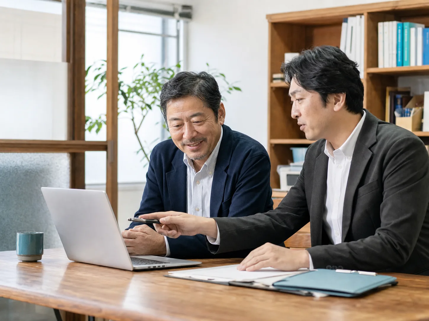 日本の中小企業の経営者と技術パートナーが、同じノートパソコンを見ながら相談している様子